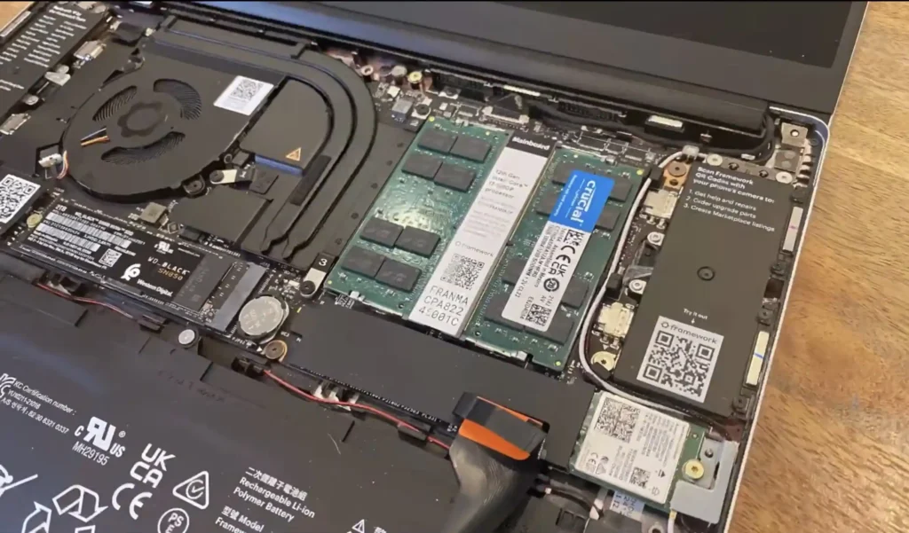 Open laptop showing internal components including RAM modules, cooling system, SSD storage, battery, and motherboard during a memory upgrade or hardware inspection.