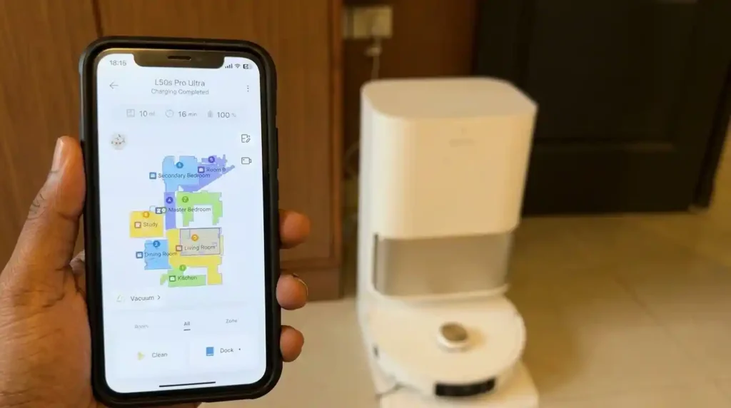 Smartphone displaying the robot vacuum app with a home map while the robot vacuum charges in its docking station.