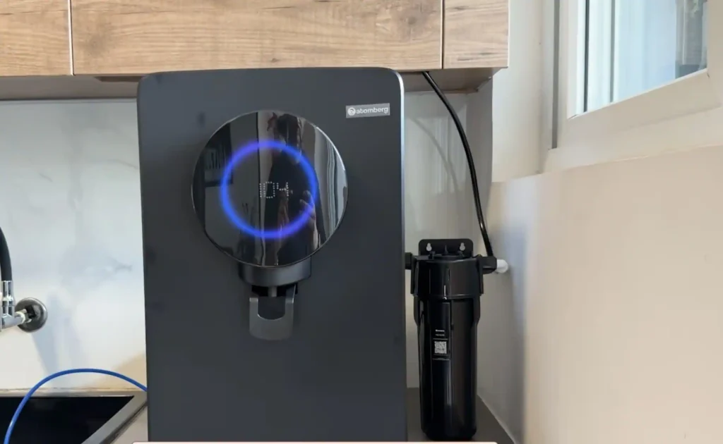 A modern black smart RO water purifier installed on a kitchen countertop with an external pre-filter and illuminated digital display.