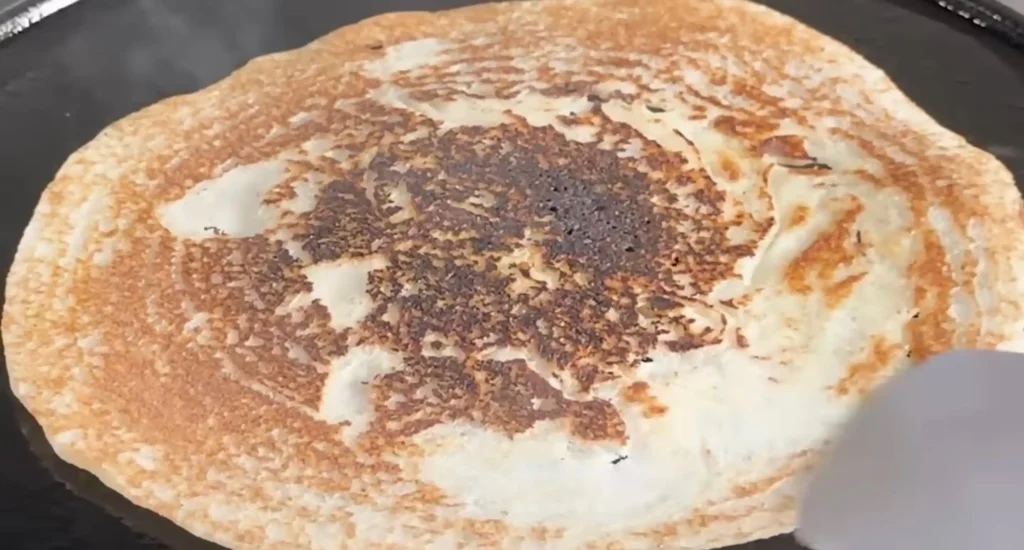 Unevenly cooked dosa with a dark centre and lighter edges, showing inconsistent heat distribution on a regular gas stove.